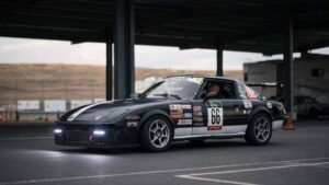 Gray Cloud Racing black #66 Mazda RX-7 with sponsor decals and Hankook tires in the paddock before a race.